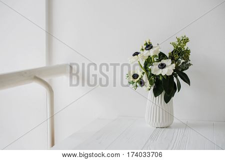 Elegant bouquet of anemones in a vase on table in white room interior, floral home dcoration