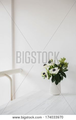 Elegant bouquet of anemones in a vase on table in white room interior, floral home dcoration