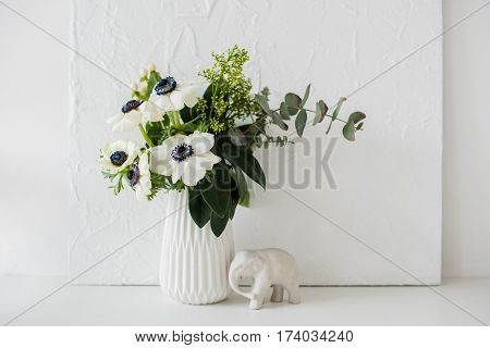 Elegant bouquet of anemones in a vase on table in white room interior, floral home dcoration