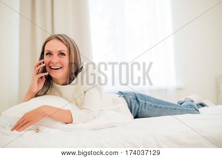A woman lies forward on her bed making a call as she smiles