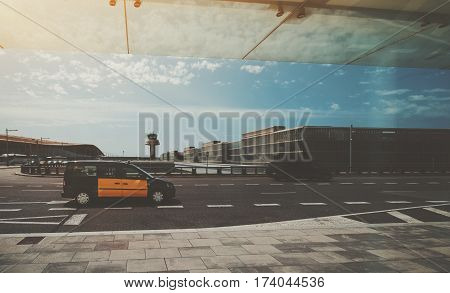 Yellow taxi on the road in front of air traffic control tower of modern contemporary airport terminal of Barcelona with buses and multiple moving blurred cars in distance on sunny day