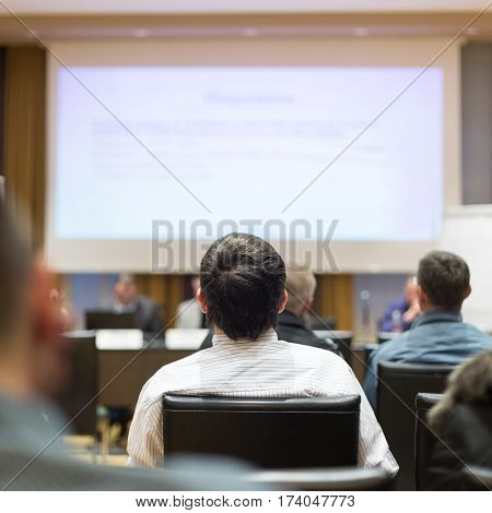 Business and entrepreneurship symposium. Speaker giving a talk at business meeting. Audience in the conference hall. Rear view of unrecognized participant in audience.