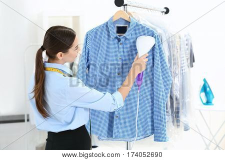 Woman with steamer cleaning clothes in dry-cleaning salon