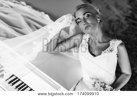 Bride Looks Marvelous Standing Behind A Piano And Holding Her Head Thoughtfull
