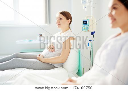 Side view of pregnant woman resting in hospital room and thinking about name for her upcoming baby