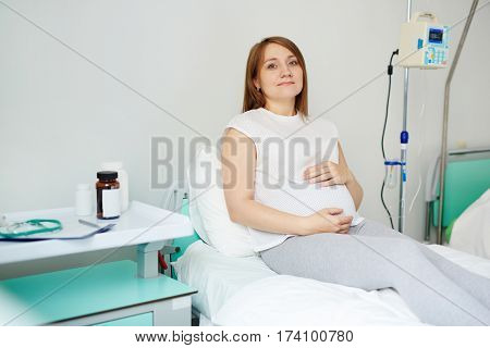 Portrait of peaceful pregnant woman resting on hospital bed before last ultrasound examination