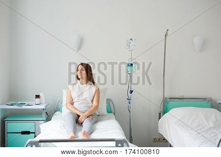 Pregnant woman lying on bed in hospital room and looking to the side thoughtfully