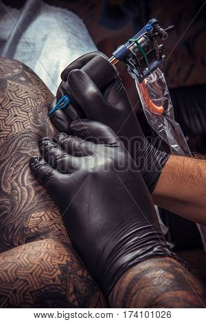 Man wearing gloves working tattooing in salon. Tattooer makes cool tattoo in tattoo studio.