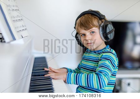 Beautiful little kid boy with headphones playing piano in living room or music school. Preschool child having fun with learning to play music instrument. Education, skills concept.
