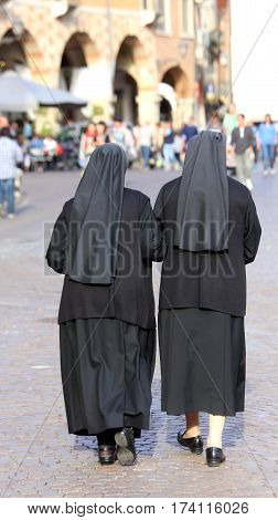 Two Sisters With Black Dresses And A Veil To Cover The Hair Walk
