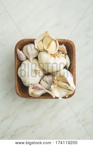 Fresh garlic in wooden bowl on kitchen table. Top view.