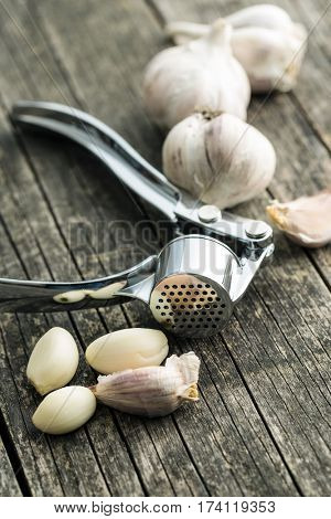 Garlic and garlic press on old wooden table.