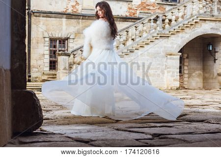 Young sexy girl with long hair and pretty face in white wedding bride dress posing near castle or palace building
