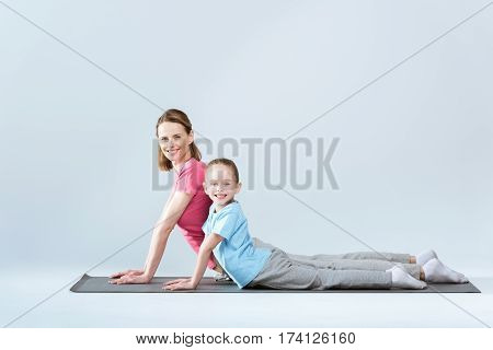Side view of smiling sporty mother and daughter practicing upward facing dog yoga pose on white