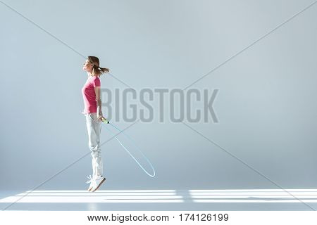 side view of sporty woman exercising with skipping rope on grey