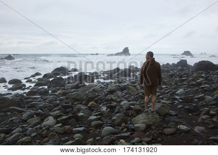 Hiker viewing picturesque wild beach with massive stones during slight storm on Tenerife, Canary Islands