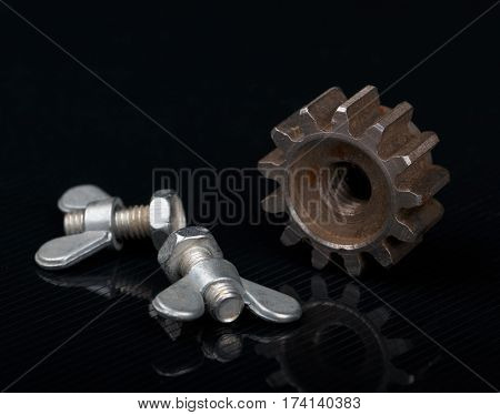 two bolts with butterfly nut and rusted gear on reflected black background