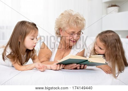 Grandmother is reading a book to her granddaughters