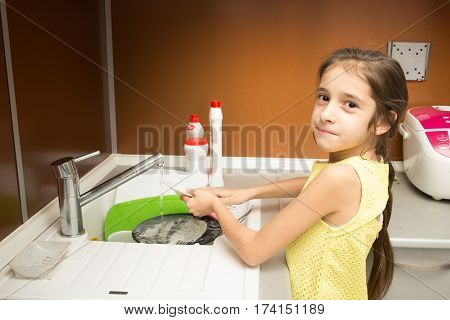 little girl makes dishes cleaning using water and sponge shot in household environment