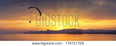 Paraglide silhouette flying above the sea against bright colorful sunset.
