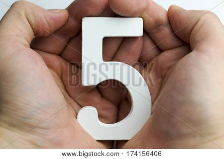 Hand holding number five on a white background.