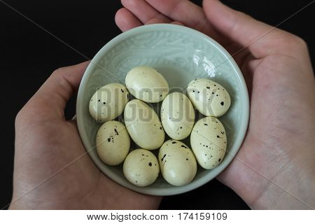 Chocolates in the form of quail eggs. Easter concept. Quail eggs in mint color plate in women hands on black background.