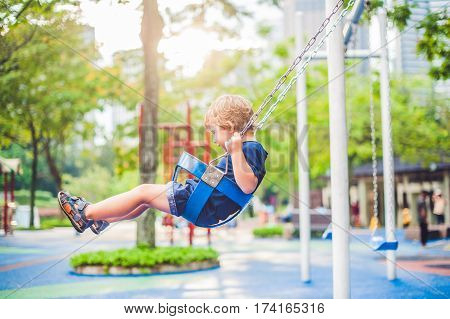Lovely Blond Little Boy On A Swing In The Park. Adorable Boy Having Fun At The Playground