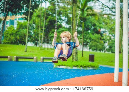 Lovely Blond Little Boy On A Swing In The Park. Adorable Boy Having Fun At The Playground