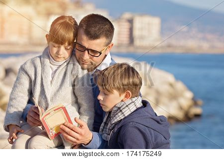 Father reading a book to his children outdoors