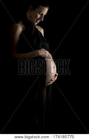 Smiling pregnant woman holding her belly isolated on black background with copyspace.