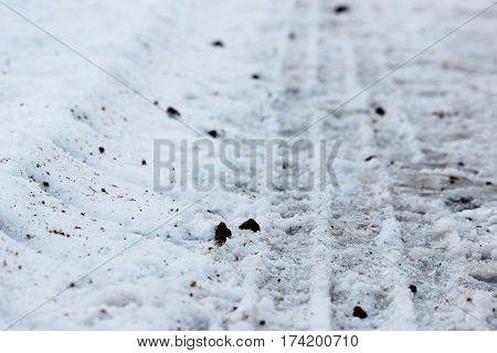 Footprints in the snow of the tractor, which threw sand on the road during icy