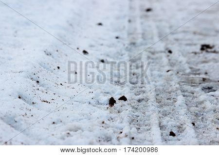 Footprints in the snow of the tractor, which threw sand on the road during icy