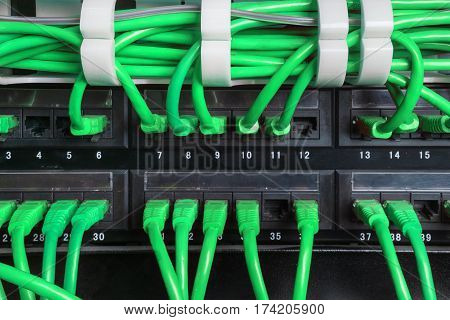 Server rack with green internet patch cord cables connected to black patch panel in server room horizontal