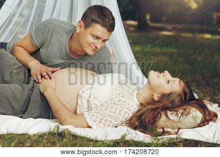 Happy Young Family, Relazing In Sunny Park, Happy Husband Holding Pregnant Wife Belly, While Looking