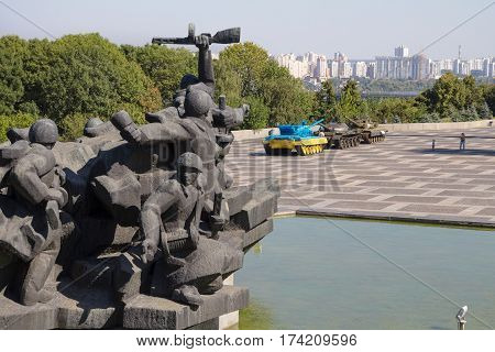 KIEV UKRAINE - AUGUST 9 2015: Communist statue in the museum of the Great Patriotic war. A Russian T55 tank captured in Eastern Ukraine by the Ukrainian army painted with the Ukrainian colors used as a trophy can be seen in Background