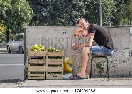 CHISINAU MOLDOVA - AUGUST 11 2015: Young man sitting on a stool selling grapes in the capital city of Moldova. Grape and fruits more generally are one of the main exports of the country