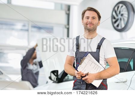 Portrait of confident male maintenance engineer with clipboard in car repair shop