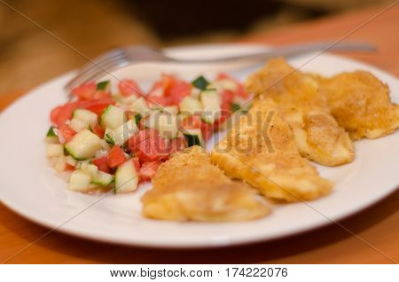 Delicious fried cheese in breadcrumbs with fresh salad of tomatoes and cucumbers