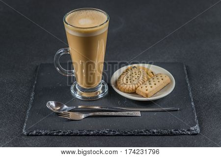 aromatic coffee latte with crispy buttered biscuits on white saucer all on a black stone plate sweet set