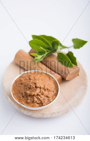 Ayurvedic Chandan powder or sandalwood paste in silver bowl with sticks and leaves placed over sahan or sahana or circular stone base for creating paste