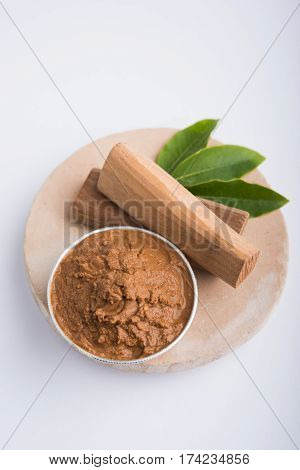 Ayurvedic Chandan powder or sandalwood paste in silver bowl with sticks and leaves placed over sahan or sahana or circular stone base for creating paste