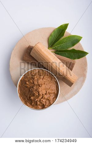 Ayurvedic Chandan powder or sandalwood paste in silver bowl with sticks and leaves placed over sahan or sahana or circular stone base for creating paste