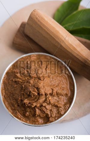 Ayurvedic Chandan powder or sandalwood paste in silver bowl with sticks and leaves placed over sahan or sahana or circular stone base for creating paste