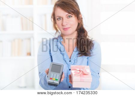 Smiling woman seller gives payment terminal and goods to the client to pay for