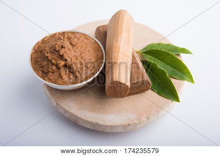 Ayurvedic Chandan powder or sandalwood paste in silver bowl with sticks and leaves placed over sahan or sahana or circular stone base for creating paste