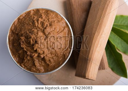 Ayurvedic Chandan powder or sandalwood paste in silver bowl with sticks and leaves placed over sahan or sahana or circular stone base for creating paste