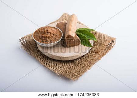 Ayurvedic Chandan powder or sandalwood paste in silver bowl with sticks and leaves placed over sahan or sahana or circular stone base for creating paste