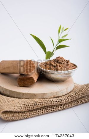 Ayurvedic Chandan powder or sandalwood paste in silver bowl with sticks and leaves placed over sahan or sahana or circular stone base for creating paste