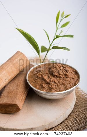 Ayurvedic Chandan powder or sandalwood paste in silver bowl with sticks and leaves placed over sahan or sahana or circular stone base for creating paste