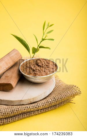 Ayurvedic Chandan powder or sandalwood paste in silver bowl with sticks and leaves placed over sahan or sahana or circular stone base for creating paste